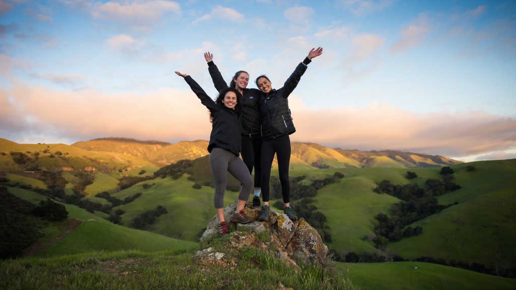 three female students reaching top of a hill