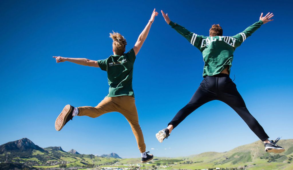 two students leap in the air and high five