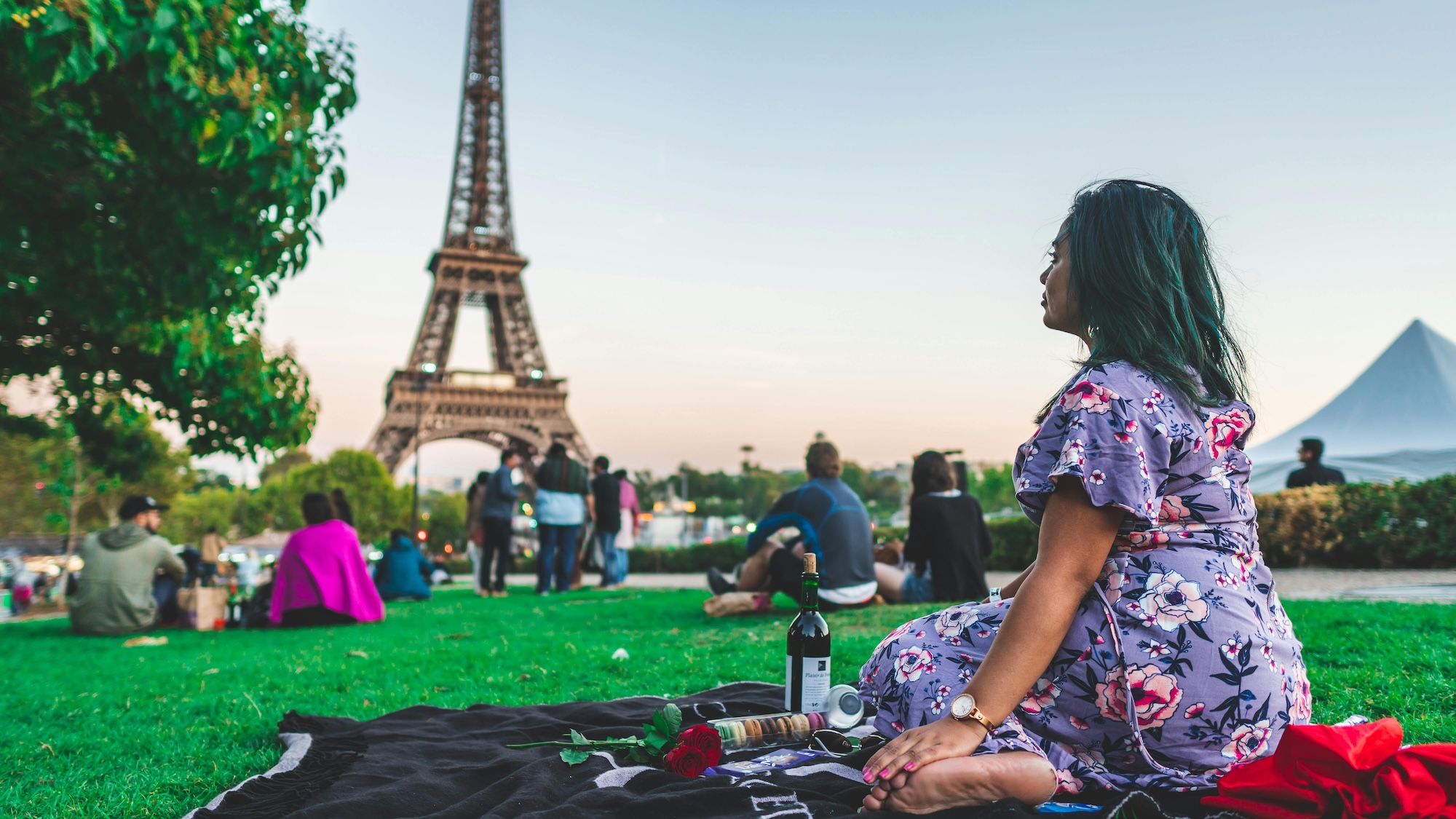 A woman sitting on a blanket, looking at the Eiffel Tower