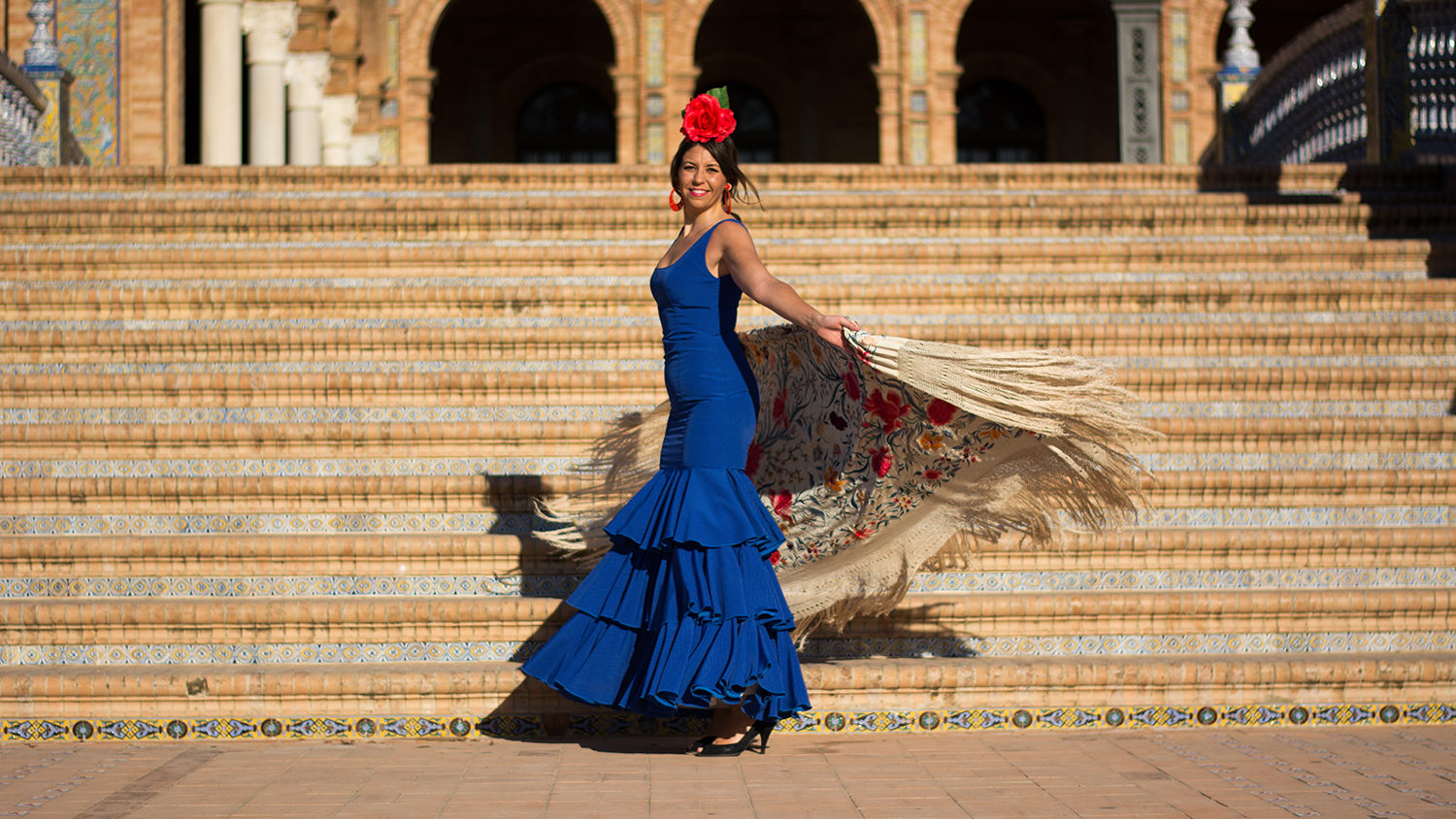 A vibrant flamenco dancer in a flowing blue dress whirls and twirls on sun-drenched steps in Seville, Spain, epitomizing the grace and passion of traditional Andalusian dance.