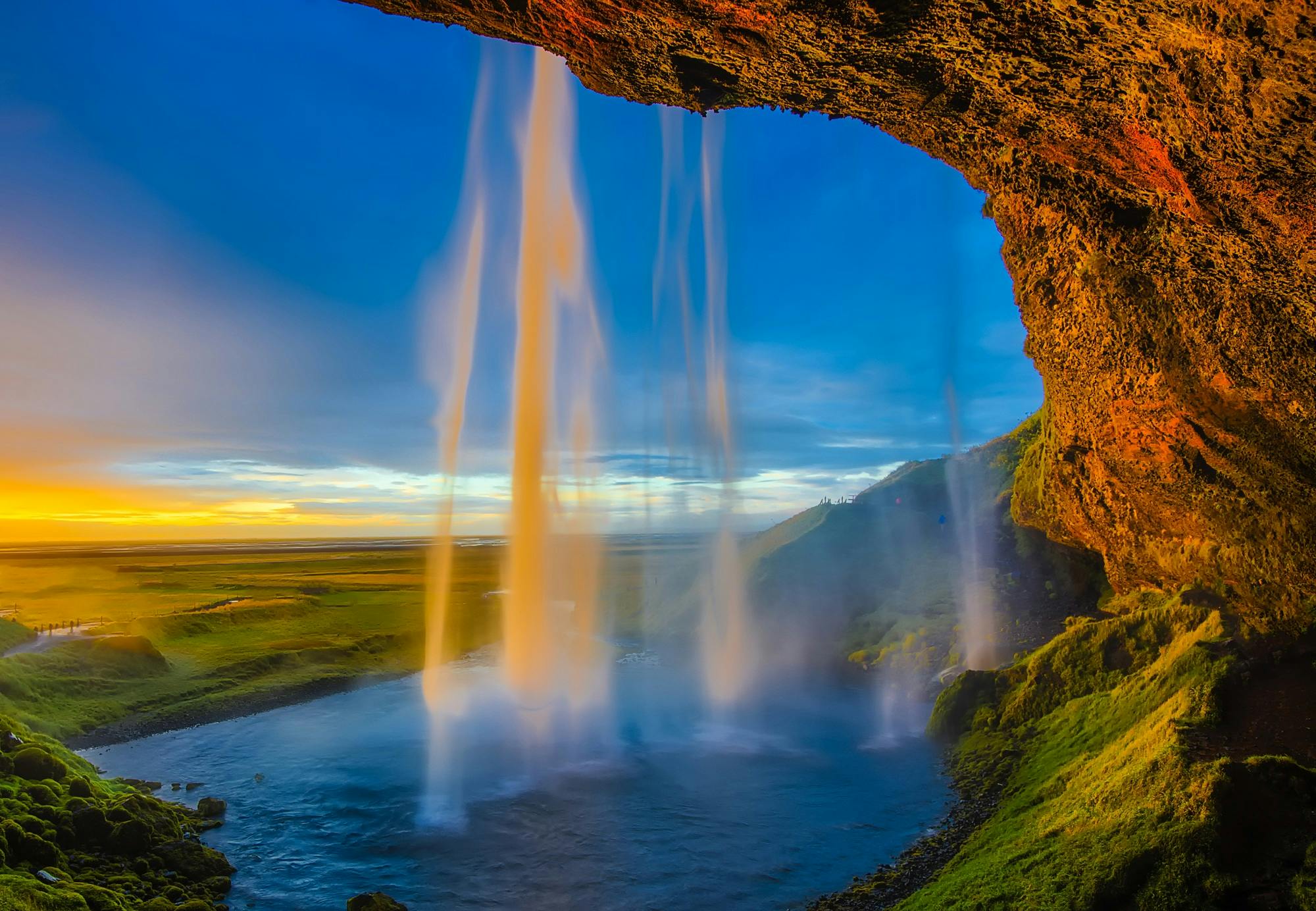 View from behind Seljalandsfoss waterfall at sunset in Iceland.