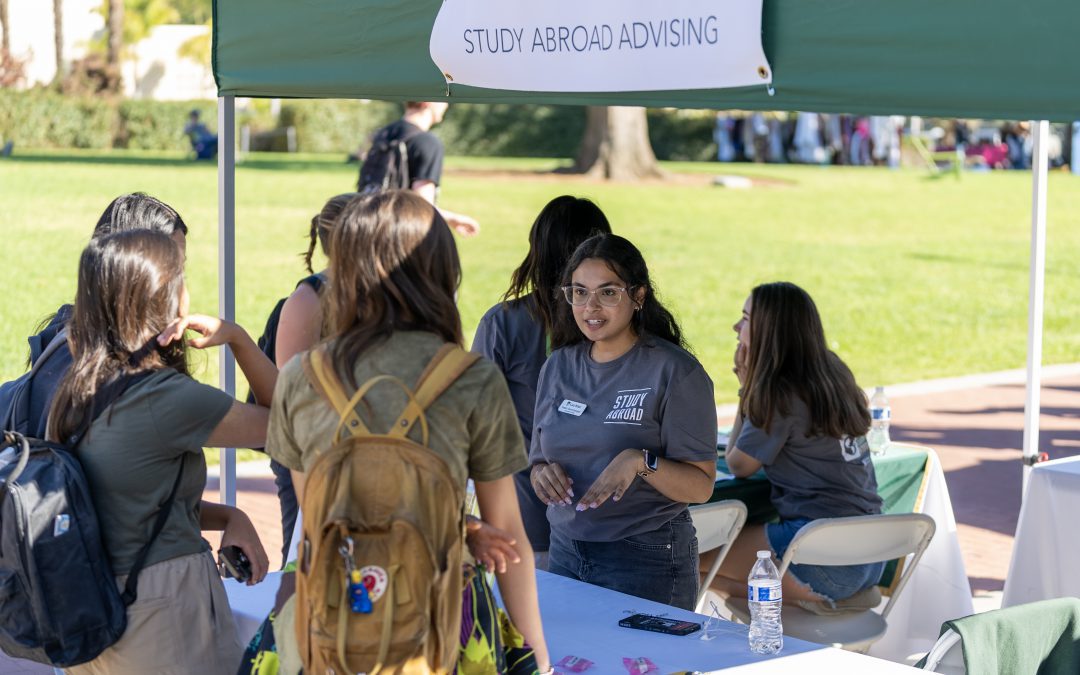 Students talking with a study abroad advisor at an outdoor campus event booth.
